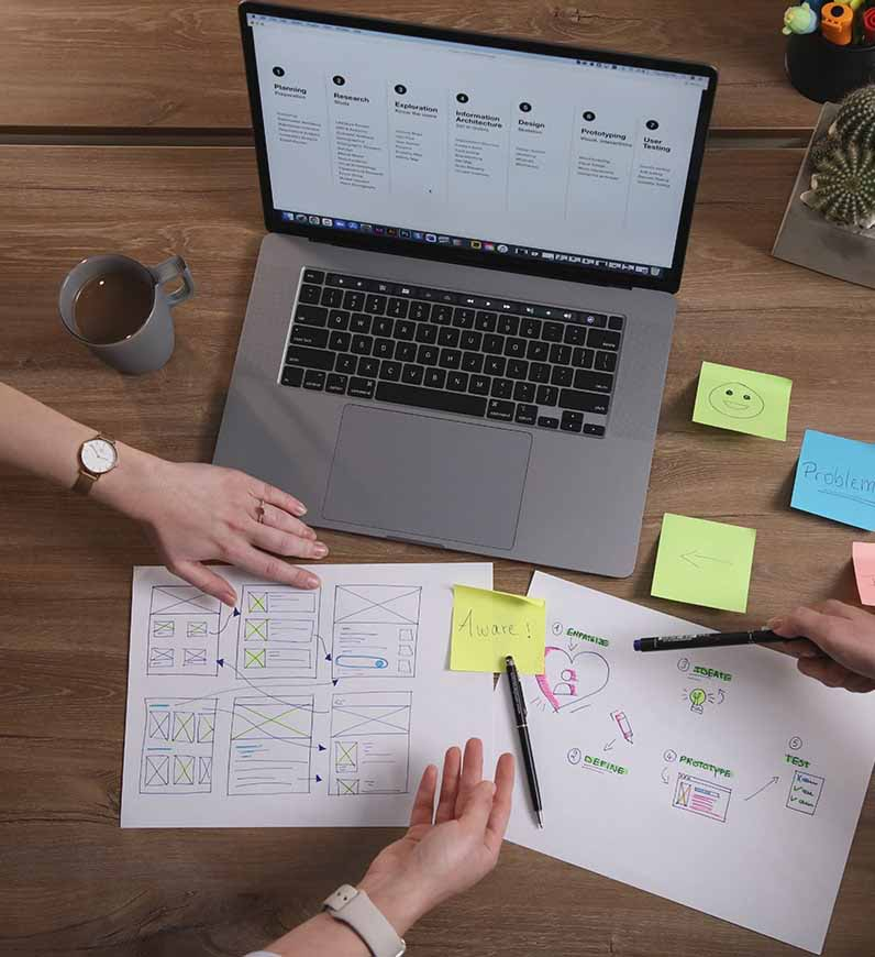 A research team is collaborating on UX research strategy that fits the client's goals using a laptop and sticky notes.